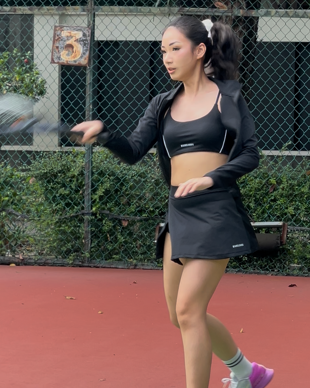 Woman playing tennis on a court Bianclouds jacket and tennis slit skort