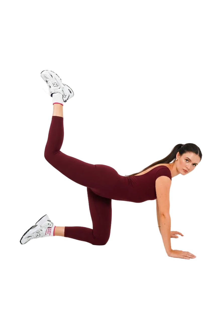 Woman in burgundy onesie and white sneakers posing pilates pose