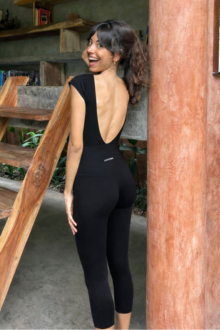 Woman wearing a black activewear jumpsuit with open back, standing outdoors near wooden stairs.